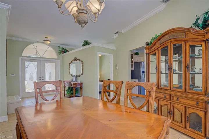 Dining space featuring french doors, ornamental molding, light tile patterned floors, and a chandelier
