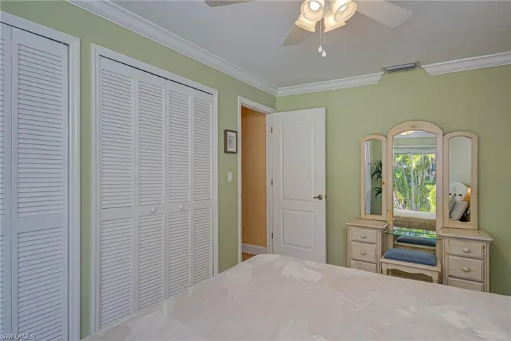 Bedroom with multiple closets, ornamental molding, visible vents, and a ceiling fan