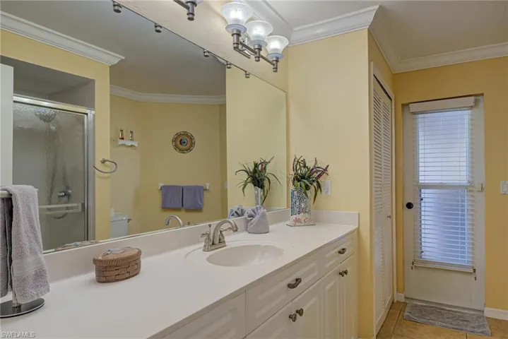Bathroom featuring a shower with shower door, ornamental molding, tile patterned floors, and vanity