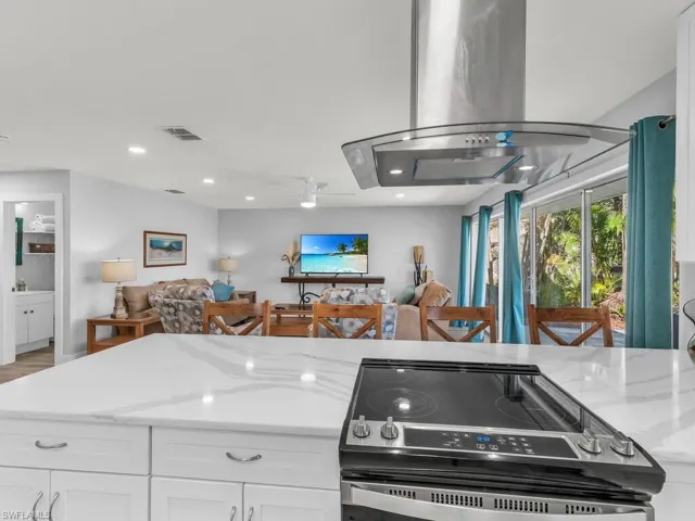 Kitchen with island range hood, white cabinets, light stone countertops, and stainless steel range oven