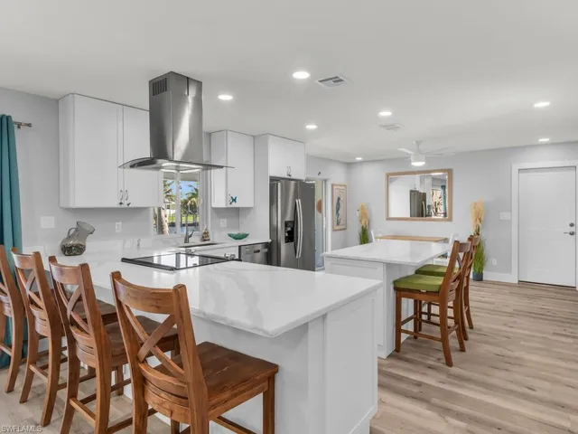 Kitchen with wall chimney exhaust hood, stainless steel fridge with ice dispenser, light hardwood / wood-style floors, a kitchen bar, and white cabinets