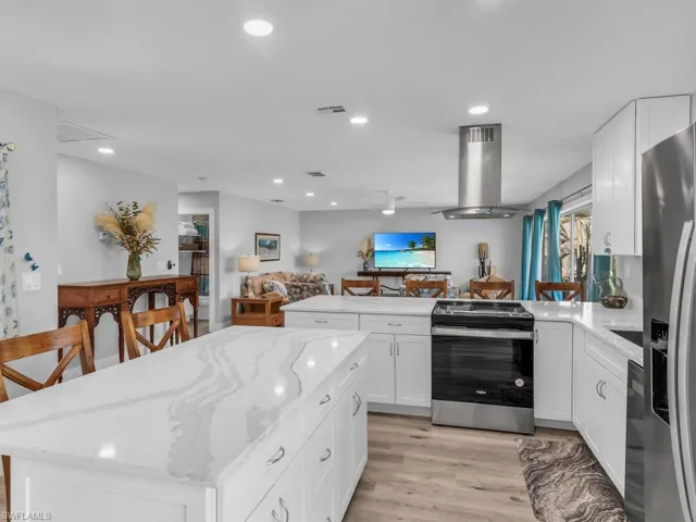 Kitchen featuring white cabinetry, light stone countertops, light hardwood / wood-style flooring, island range hood, and appliances with stainless steel finishes