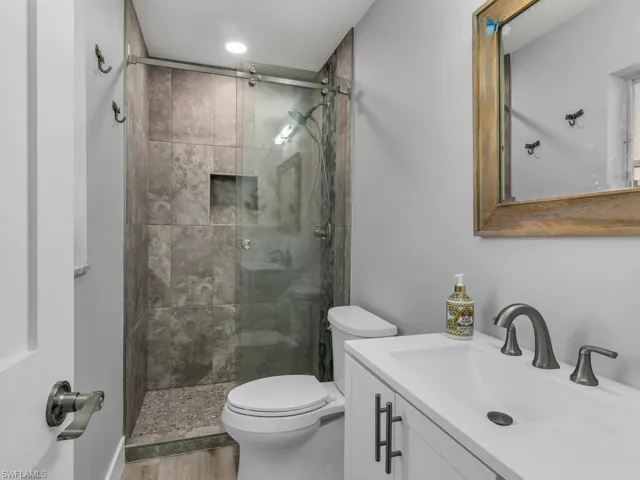 Bathroom featuring a shower with shower door, toilet, wood-type flooring, and vanity