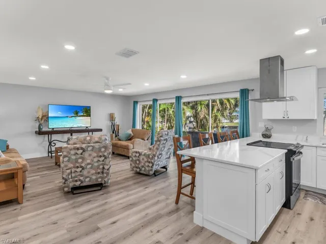 Kitchen with ceiling fan, range hood, white cabinets, light hardwood / wood-style floors, and stainless steel electric range