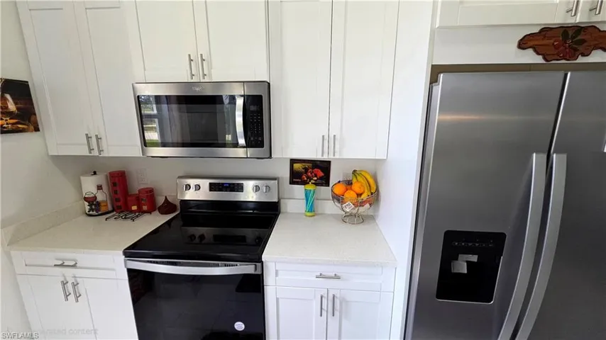 Kitchen featuring stainless steel appliances, white cabinets, and light stone countertops
