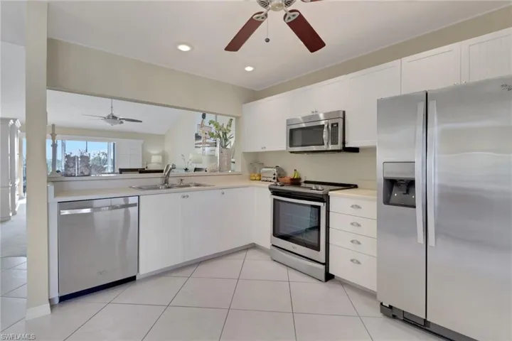 Kitchen with appliances with stainless steel finishes, white cabinetry, light countertops, open floor plan, and ceiling fan