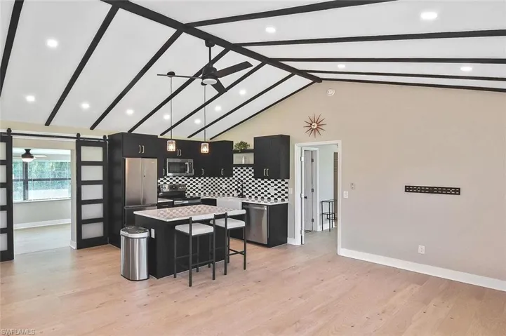 Kitchen featuring a ceiling fan, dark cabinets, a kitchen bar, beamed ceiling, and high vaulted ceiling