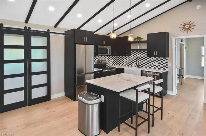 Kitchen featuring dark cabinets, a barn door, beamed ceiling, a kitchen bar, and decorative light fixtures