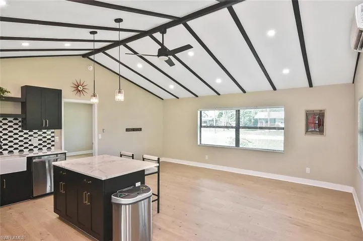 Kitchen featuring dark cabinets, pendant lighting, a kitchen bar, open floor plan, and beam ceiling