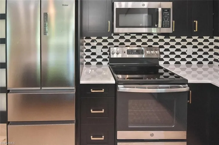 New stainless appliances and a geometric black-and-white backsplash beautifully accent the rich dark cabinetry and bright white quartz countertops.