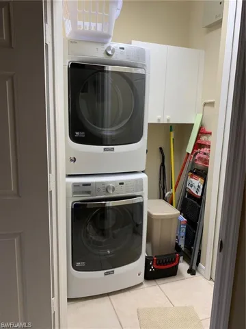 Laundry room featuring light tile patterned flooring, stacked washer and clothes dryer, and cabinet space