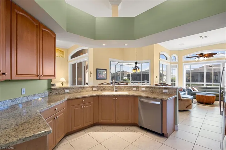 Kitchen featuring open floor plan, light stone countertops, dishwasher, a peninsula, and a ceiling fan