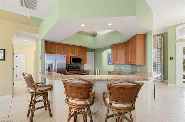 Kitchen featuring a kitchen bar, ornamental molding, light tile patterned flooring, stainless steel appliances, and a raised ceiling