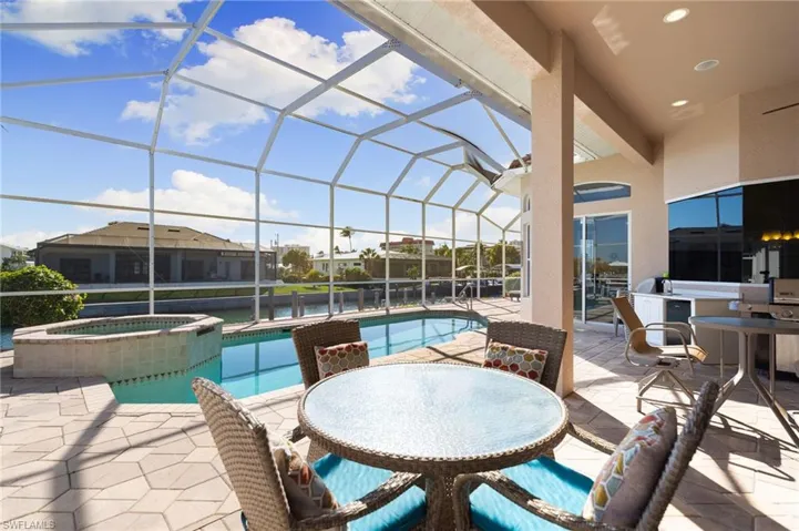 Combined pool / hot tub with a sunroom, a patio area, glass enclosure, and an outdoor kitchen / dining area