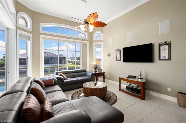 Living room with crown molding, ceiling fan, light tile patterned floors, and a high ceiling