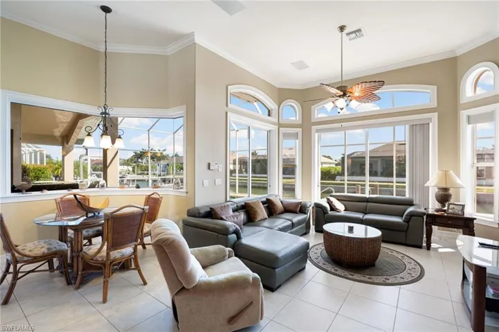 Living area with healthy amount of natural light, light tile patterned flooring, ornamental molding, a ceiling fan, and a high ceiling