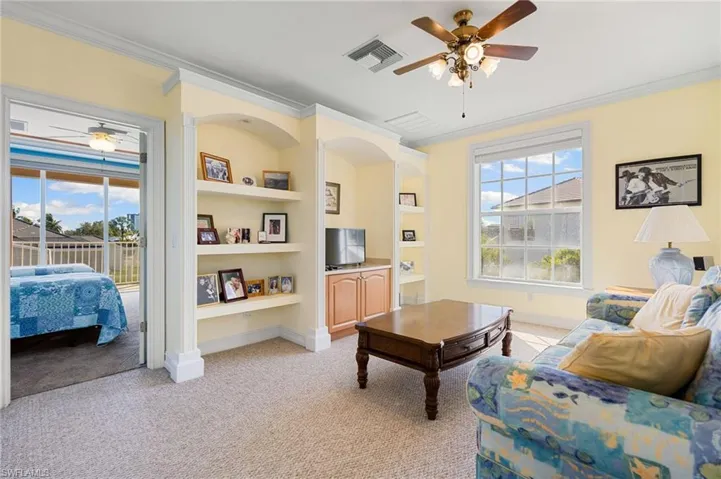 Living room featuring ceiling fan, ornamental molding, light carpet, and built in shelves