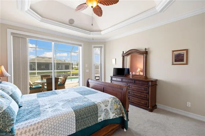 Bedroom featuring access to exterior, ceiling fan, carpet flooring, ornamental molding, and a tray ceiling