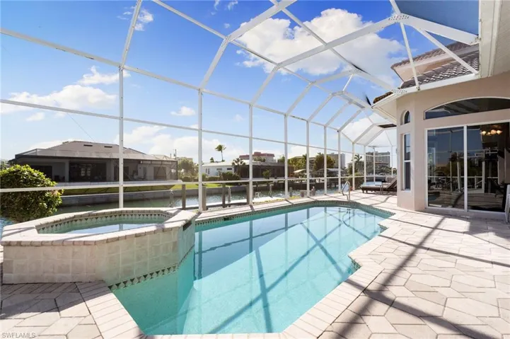 Combined pool / hot tub featuring a lanai, a patio area, a sunroom, and a water view