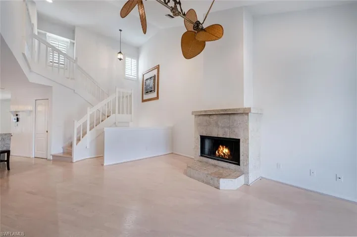 Unfurnished living room with light hardwood / wood-style floors, a high ceiling, a tiled fireplace, and ceiling fan
