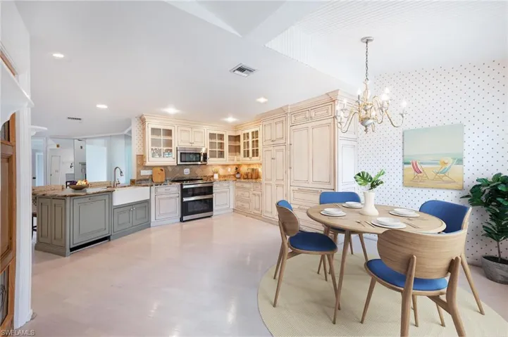 Kitchen with cream cabinetry, decorative backsplash, light stone countertops, stainless steel appliances, and decorative light fixtures
