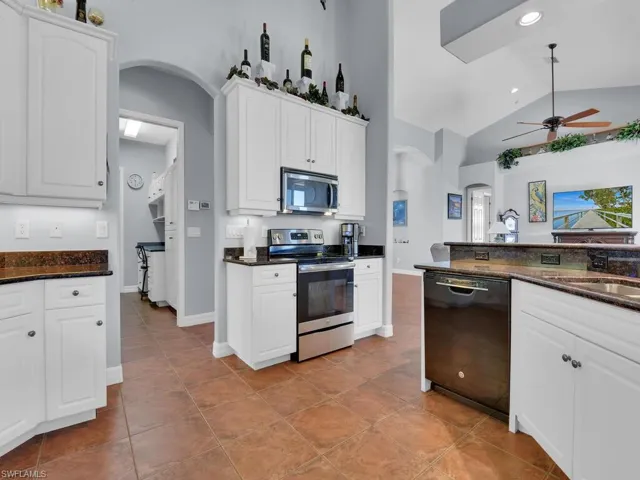Kitchen featuring dark stone counters, ceiling fan, light tile patterned floors, white cabinetry, and stainless steel appliances