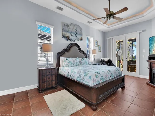 Bedroom featuring access to exterior, french doors, a tray ceiling, dark tile patterned floors, and ceiling fan