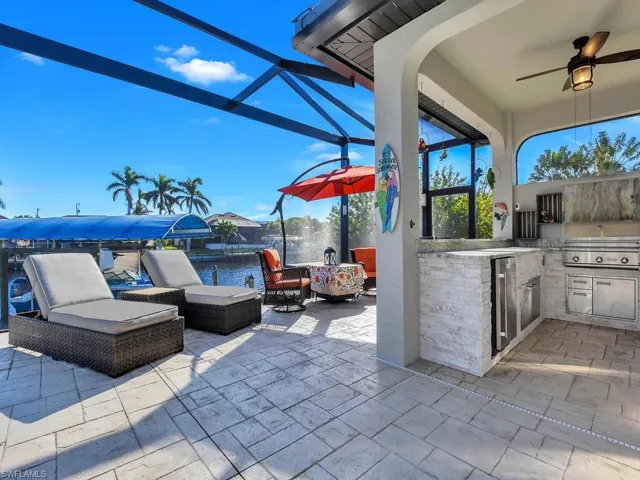 View of patio featuring area for grilling, a lanai, ceiling fan, exterior kitchen, and a water view