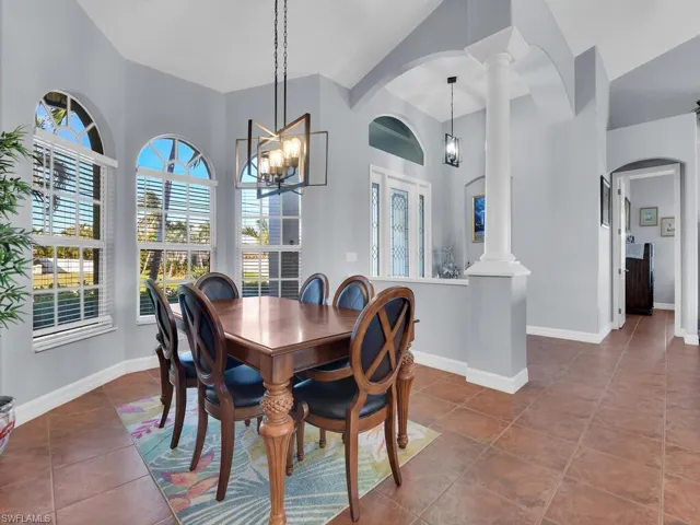 Tiled dining space featuring a towering ceiling, decorative columns, and an inviting chandelier
