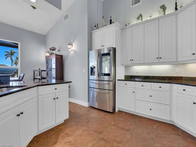 Kitchen featuring stainless steel fridge with ice dispenser, white cabinetry, dark stone counters, and light tile patterned flooring