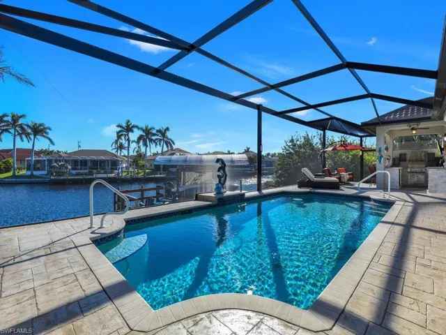 View of swimming pool featuring glass enclosure, a patio area, exterior kitchen, and a water view