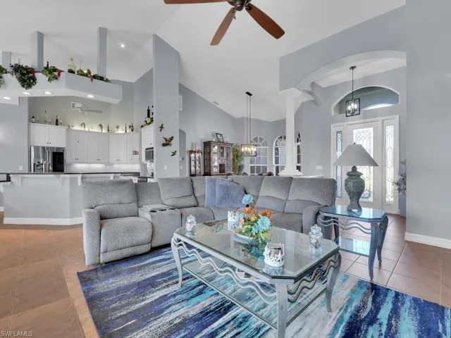Tiled living room with ceiling fan with notable chandelier and high vaulted ceiling