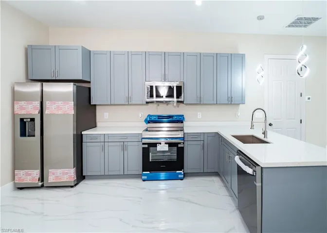 Kitchen featuring a peninsula, stainless steel appliances, decorative light fixtures, light marble finish floors, and gray cabinetry
