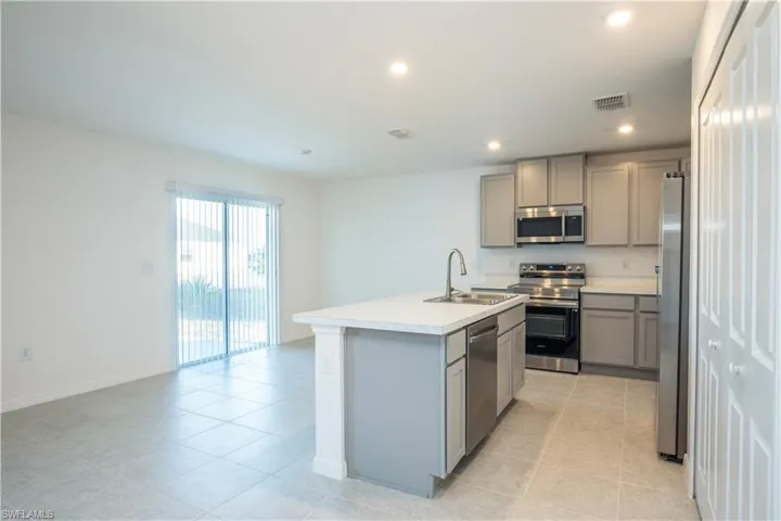 Kitchen featuring sink, gray cabinets, stainless steel appliances, and an island with sink
