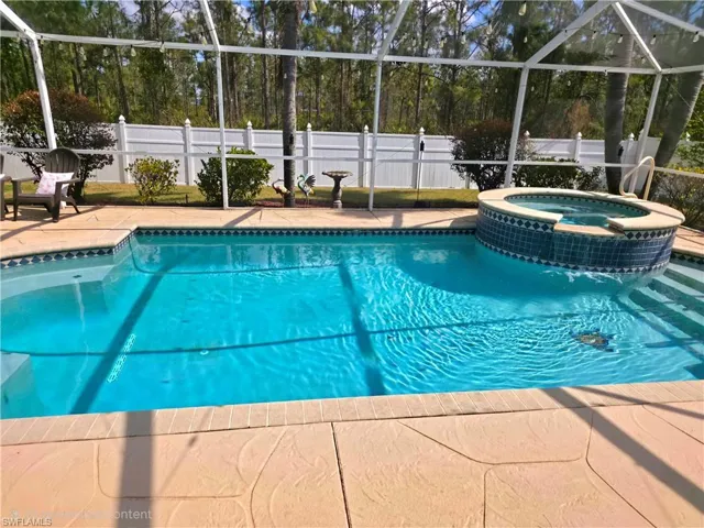 Relaxing pool / spa with glass enclosure, a fenced backyard, and a patio area