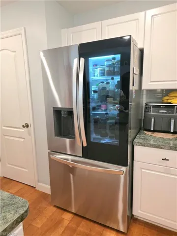 Kitchen featuring stainless steel refrigerator with ice dispenser, white cabinetry, light wood finished floors, and dark stone counters