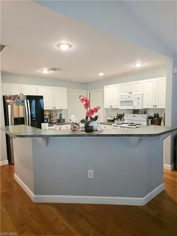 Kitchen with a large island, white cabinetry, a kitchen breakfast bar, dark wood finished floors, and recessed lighting
