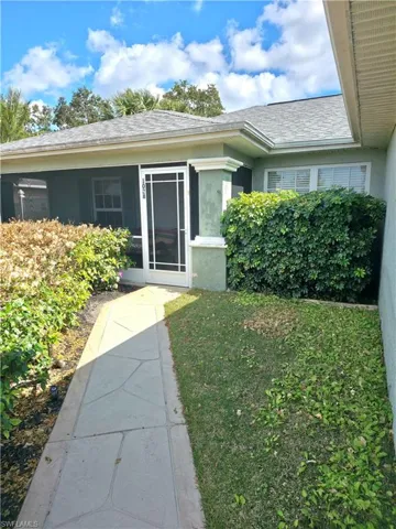 View of exterior entry featuring a yard, stucco siding, roof with shingles, and a sunroom