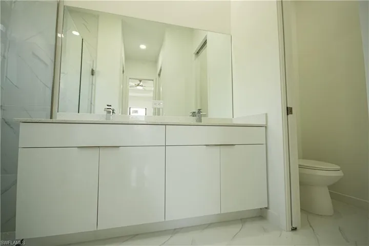Full bath featuring a sink, double vanity, toilet, marble finish floor, and baseboards