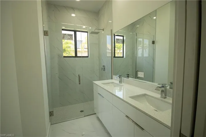 Full bath with a sink, a marble finish shower, double vanity, and marble finish floor