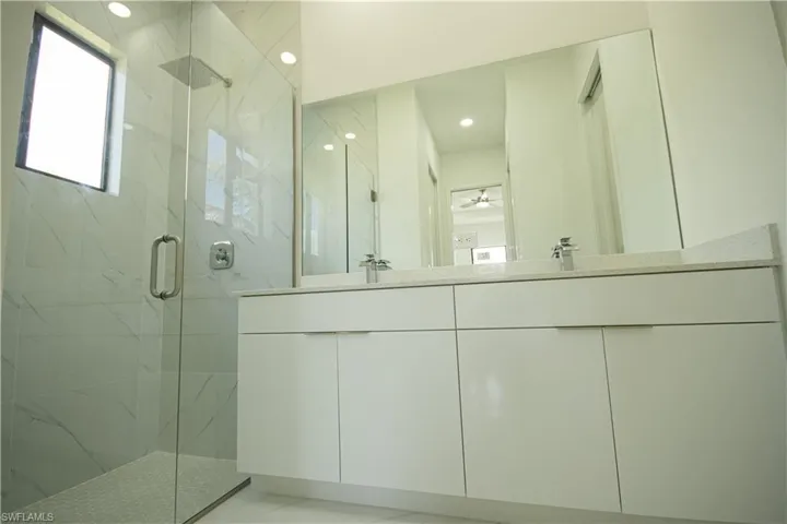 Bathroom featuring double vanity, a sink, recessed lighting, and a marble finish shower