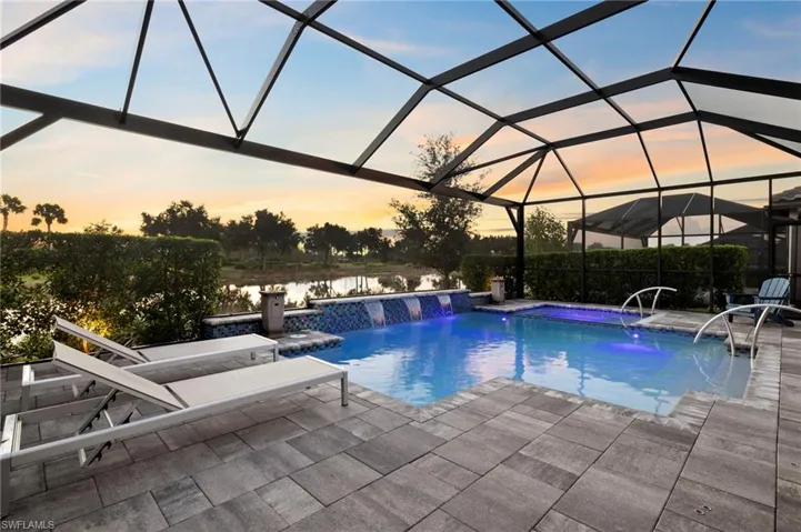 Pool at dusk featuring a jacuzzi, a patio area, pool water feature, a water view, and a lanai