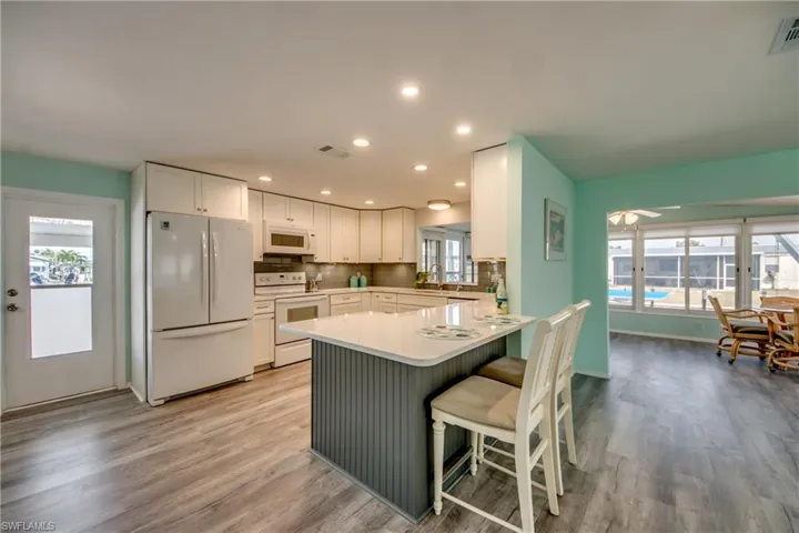 Kitchen with white appliances, light wood-type flooring, white cabinets, decorative backsplash, and recessed lighting