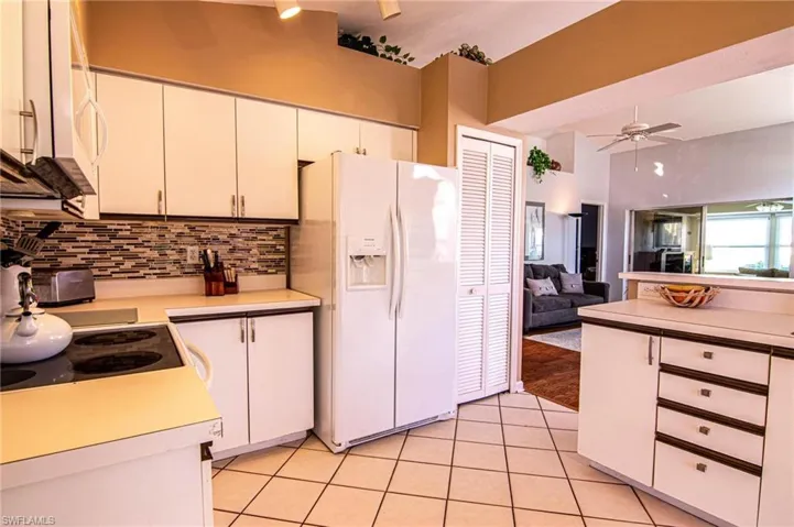Kitchen with decorative backsplash, white appliances, ceiling fan, white cabinetry, and light tile patterned flooring