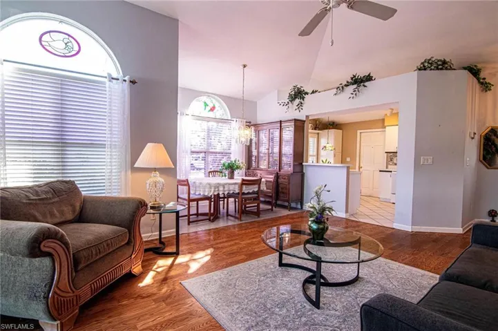 Living room featuring ceiling fan with notable chandelier, light hardwood / wood-style floors, and vaulted ceiling