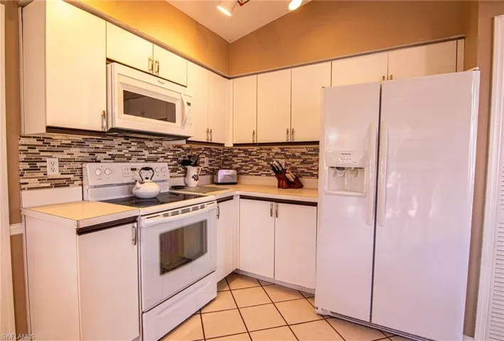 Kitchen featuring white cabinetry, white appliances, and backsplash