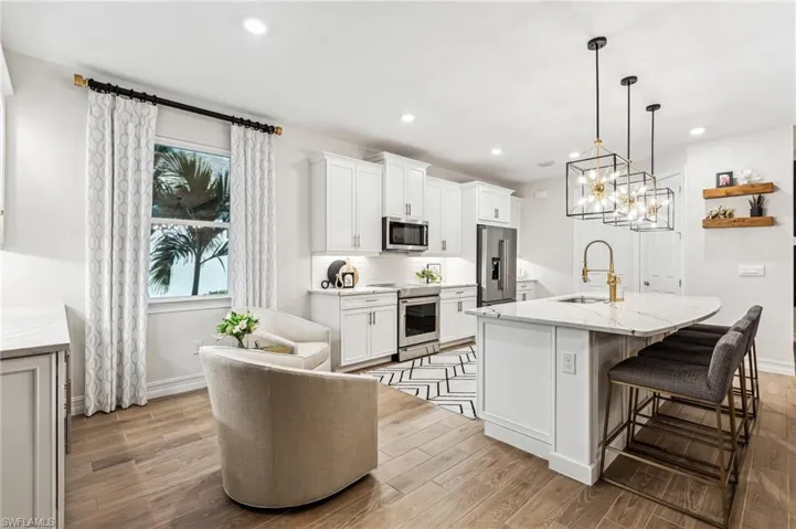 Kitchen with light stone counters, stainless steel appliances, a center island with sink, white cabinets, and hanging light fixtures