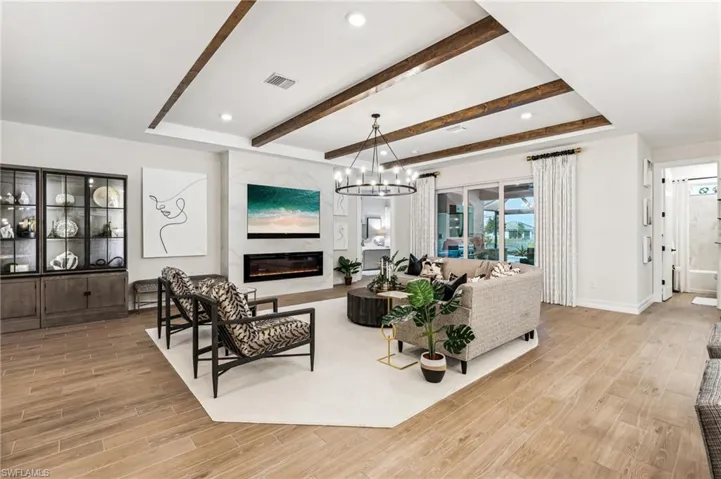 Living room with a high end fireplace, light hardwood / wood-style floors, an inviting chandelier, and beamed ceiling