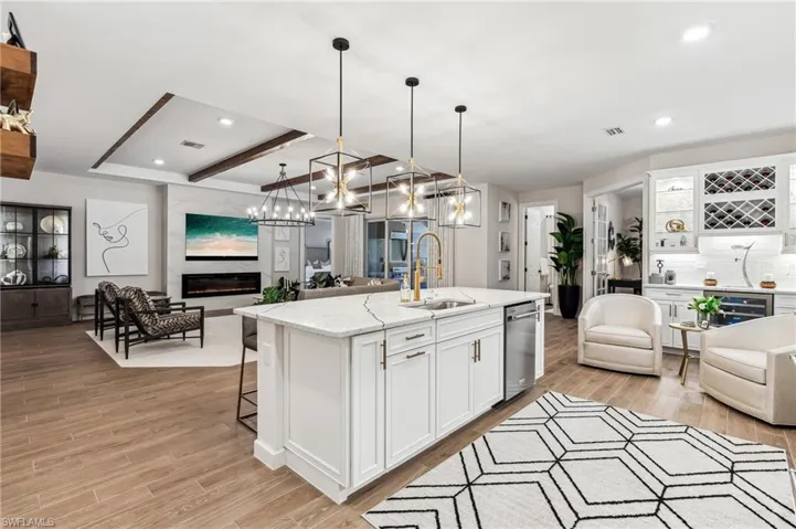 Kitchen featuring white cabinetry, sink, dishwasher, pendant lighting, and a center island with sink