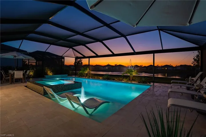 Pool at dusk with glass enclosure, an in ground hot tub, a water view, and a patio